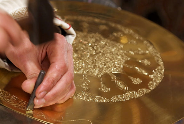 An artisan's hand skillfully crafts a brass product using traditional tools.