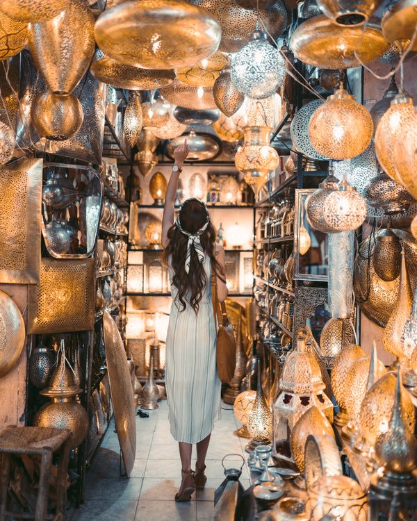 A girl standing inside a Moroccan lamp shop surrounded by colorful lamps.