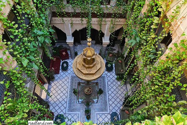 Above view of a riad courtyard showcases a fountain, hanging plants, and a large central chandelier