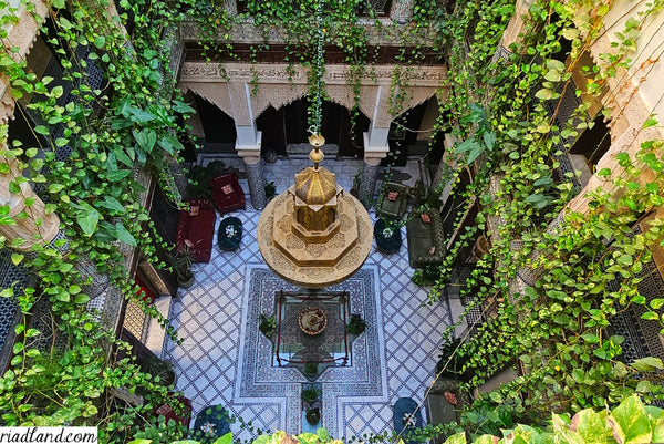 Above view of a riad courtyard showcases a fountain, hanging plants, and a large central chandelier