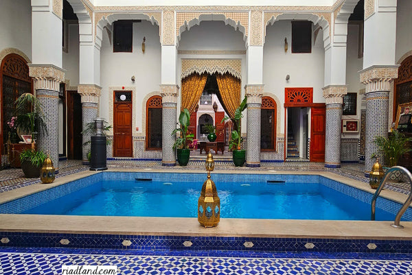 Riad courtyard featuring a serene pool surrounded by colorful zellige tiles, pillars and floor lamps