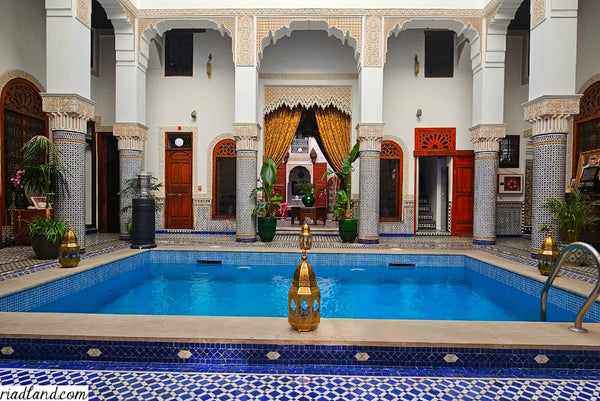 Riad courtyard featuring a serene pool surrounded by colorful zellige tiles, pillars and floor lamps