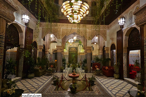 Evening atmosphere inside a riad with one large hanging lamp above the fountain