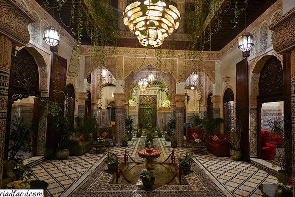 Evening atmosphere inside a riad with one large hanging lamp above the fountain