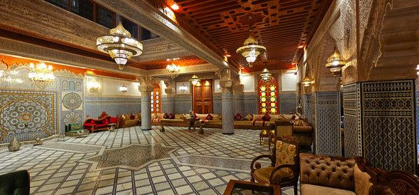 Detailed riad interior with Moroccan architecture, showcasing pillars and a grand ceiling adorned with impressive hanging lamps.