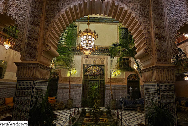 Cozy riad at night, showcasing a large hanging lamp behind a arched-wall with vibrant plants