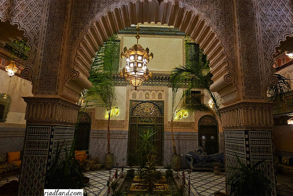 Cozy riad at night, showcasing a large hanging lamp behind a arched-wall with vibrant plants