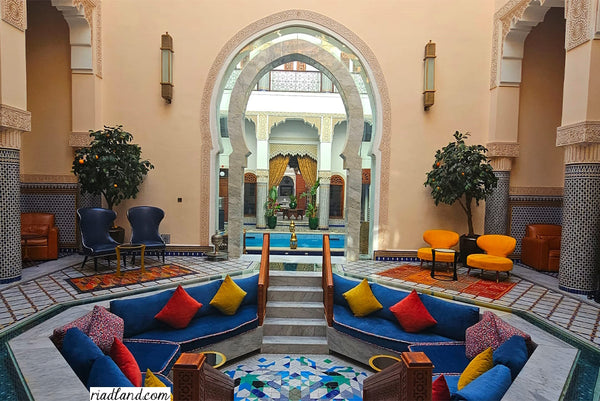 Colorful seating area in a riad with vibrant pilllows overlooking a large entrance gate with swimming pool