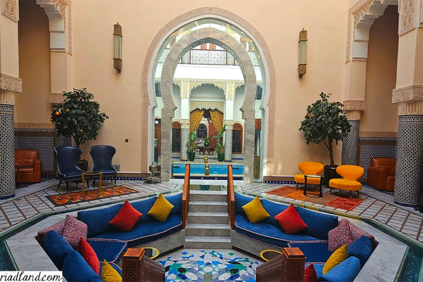 Colorful seating area in a riad with vibrant pilllows overlooking a large entrance gate with swimming pool