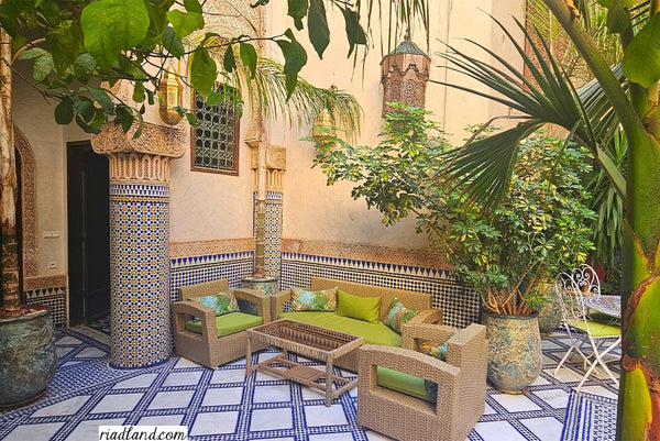 Cozy outdoor Lounge in a riad garden with light green accents, surrounded by tropical plants and pillars with zellige tiles