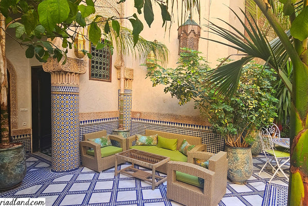 Cozy outdoor Lounge in a riad garden with light green accents, surrounded by tropical plants and pillars with zellige tiles