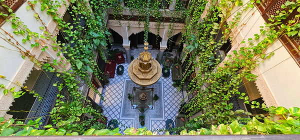 Above view of a riad courtyard showcases a fountain, hanging plants, and a large central chandelier.