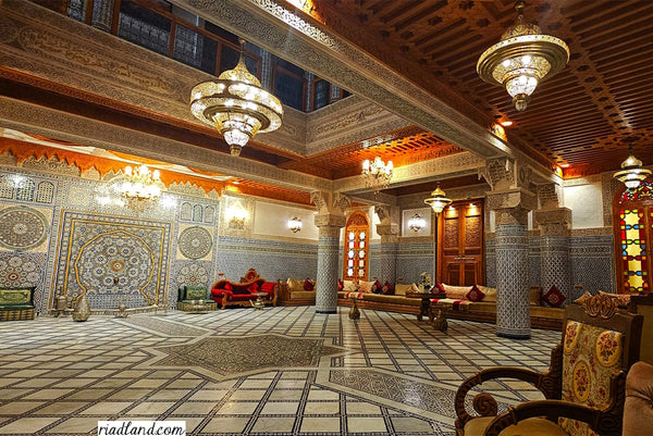 Detailed riad interior with Moroccan architecture, showcasing pillars and a grand ceiling adorned with impressive hanging lamps