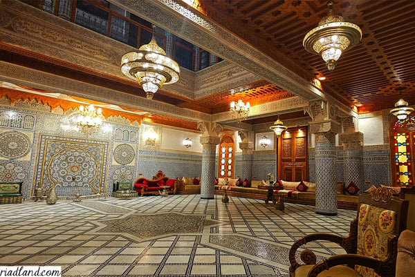 Detailed riad interior with Moroccan architecture, showcasing pillars and a grand ceiling adorned with impressive hanging lamps